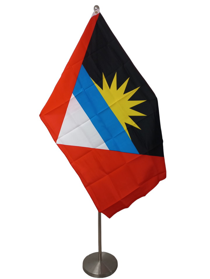 Flag of Antigua and Barbuda featuring vertical stripes in black, red, and white with a yellow sun and rays design on the red stripe. On a ceremonial flagpole.