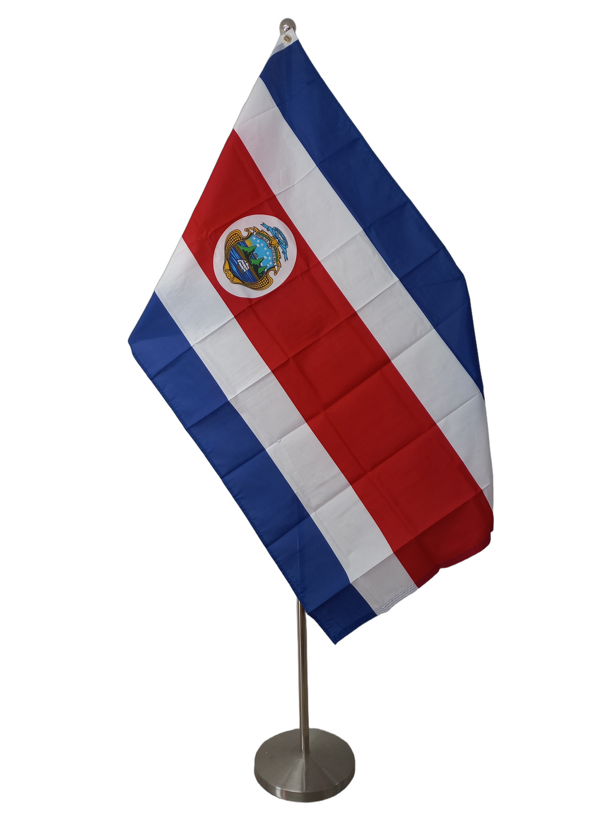 The flag of Costa Rica, featuring central red horizontal stripe with blue and white stripes above and below the red stripe. On the mid left of the red stripe there is a white oval with the Costa Rican coat of arms. On a ceremonial flag pole.