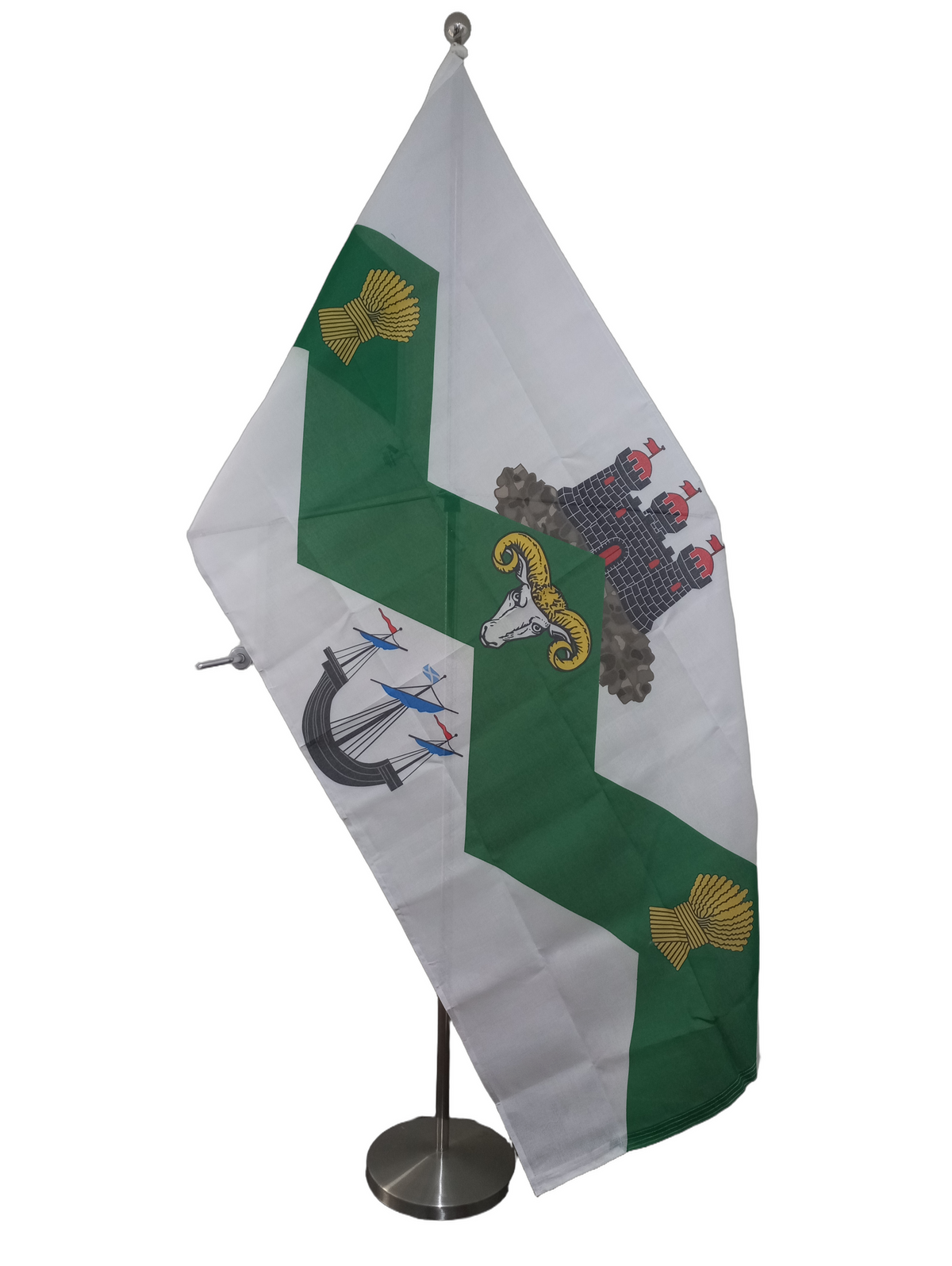 White flag with a green zig-zag pattern from left to right. Bellow the green is a black ship, above is a castle, in the center there is a rams head and on either side is a bail of wheat. On a ceremonial flag pole.
