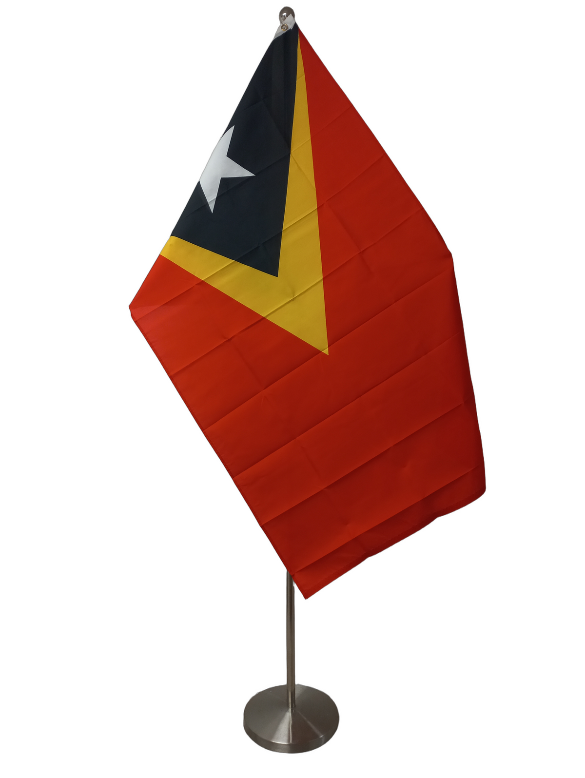 The flag of East Timor, featuring a red background with a yellow triangle and within the triangle a black triangle with a white star on it. Both triangles span the header. On a ceremonial flag pole.